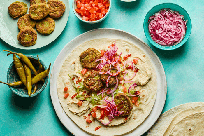 Plate with wrap topped with hummus and falafel with sliced red onion on the side