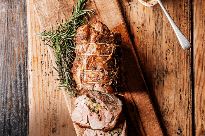 Tarragon and anchovy stuffed lamb shoulder on a wooden chopping board with sprigs of tarragon