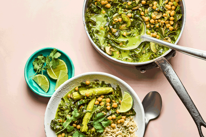 Two bowls of spring greens coconut curry with wedges of lime on the side