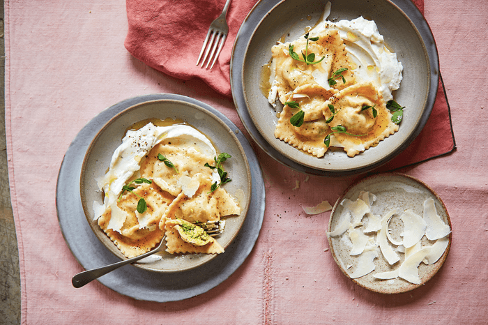 two plates of ravioli with creamy whipped ricotta and parmesan shavings on a pink tablecloth