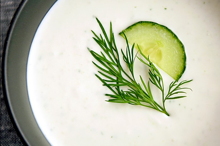 A close up of a bowl of white soup topped with a slice of green cucumber and sprig of dill